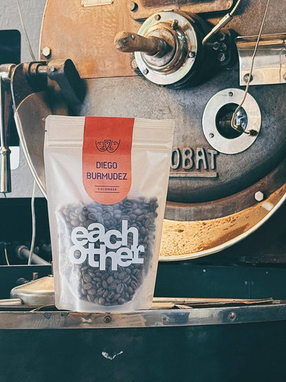 A bag of Diego Burmudez coffee beans by Eachother, placed in front of a vintage coffee roaster.